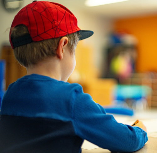 a young boy sitting at a table writing on a piece of paper
